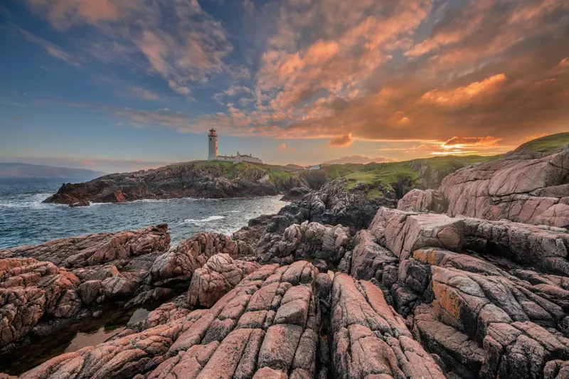 Weathered coastal rocks leading toward a lighthouse at dusk