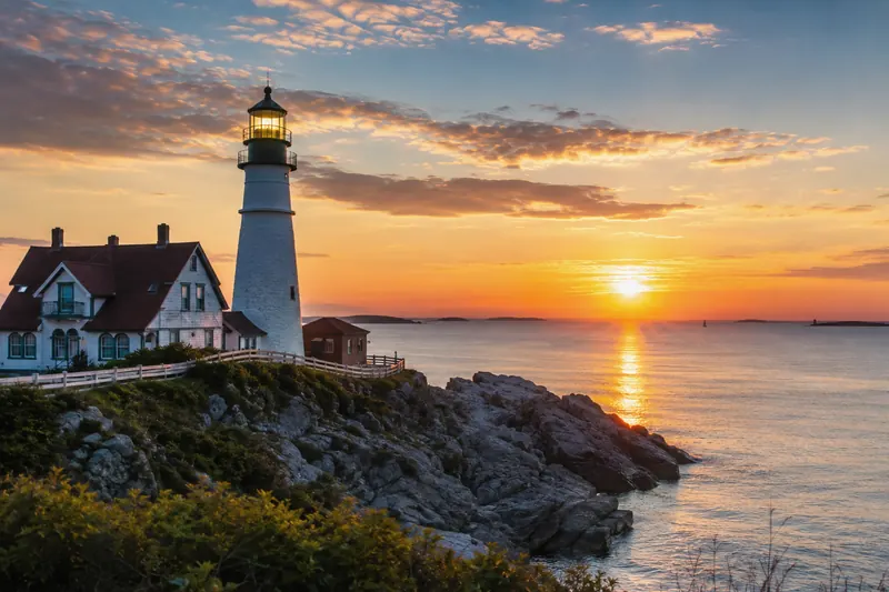 A lighthouse and cottage on a rocky coast in evening light