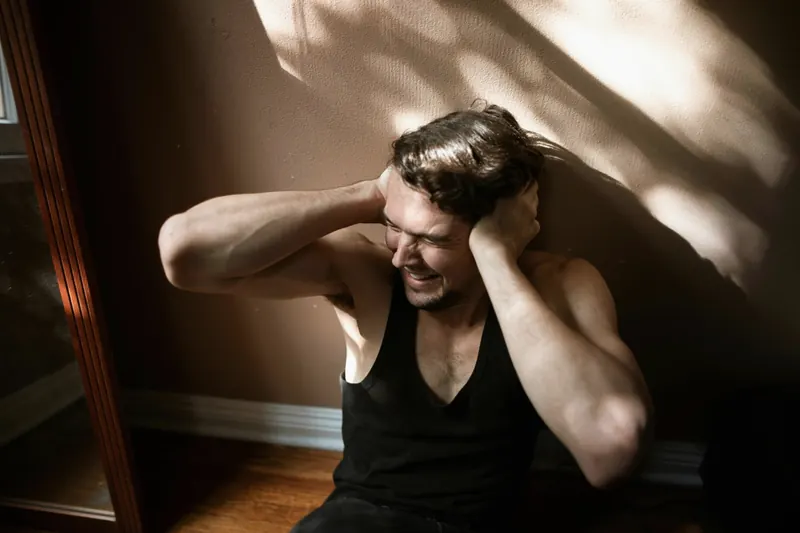 A distressed young man holding his head in a dim room