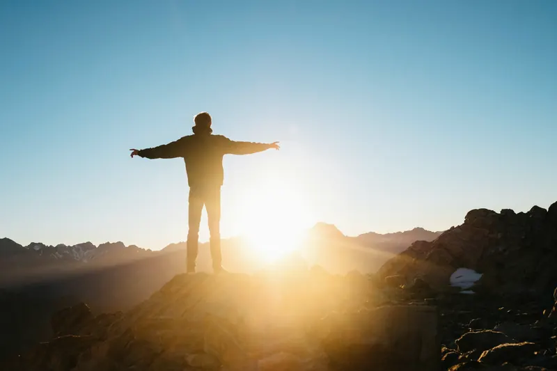 A person standing on a hilltop with arms open to the sunrise