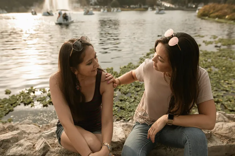 Two women talking and comforting each other beside a lake