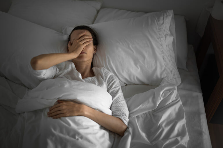 Woman lying down in bed feeling sick, headache, stomachache