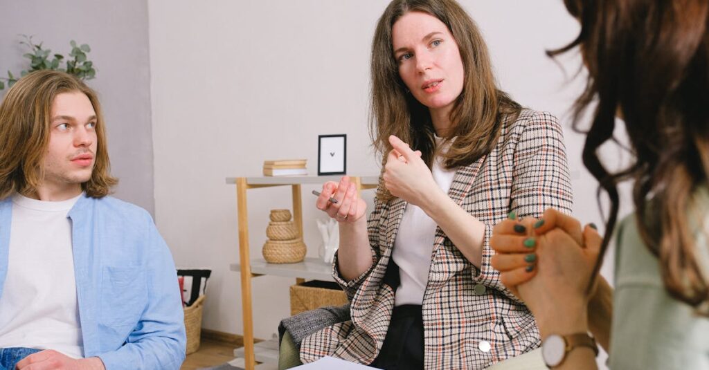 Thoughtful woman psychologist in stylish clothes siting with clipboard and talking with couple in light room